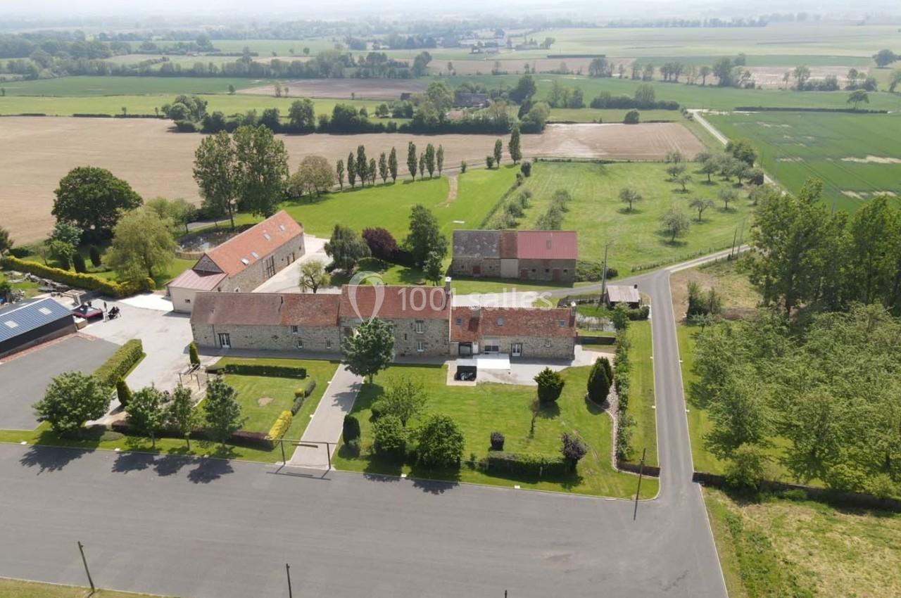 Vue aérienne d'un ensemble de bâtiments en pierre avec toits rouges, entourés de champs et d'arbres.