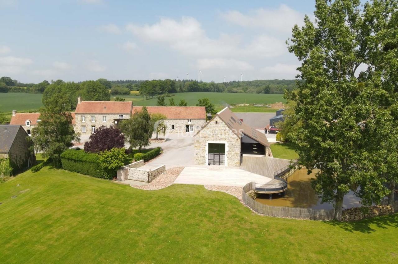 Vue aérienne d'un domaine rural avec bâtiments en pierre, pelouse, arbres et un petit étang adjacent.