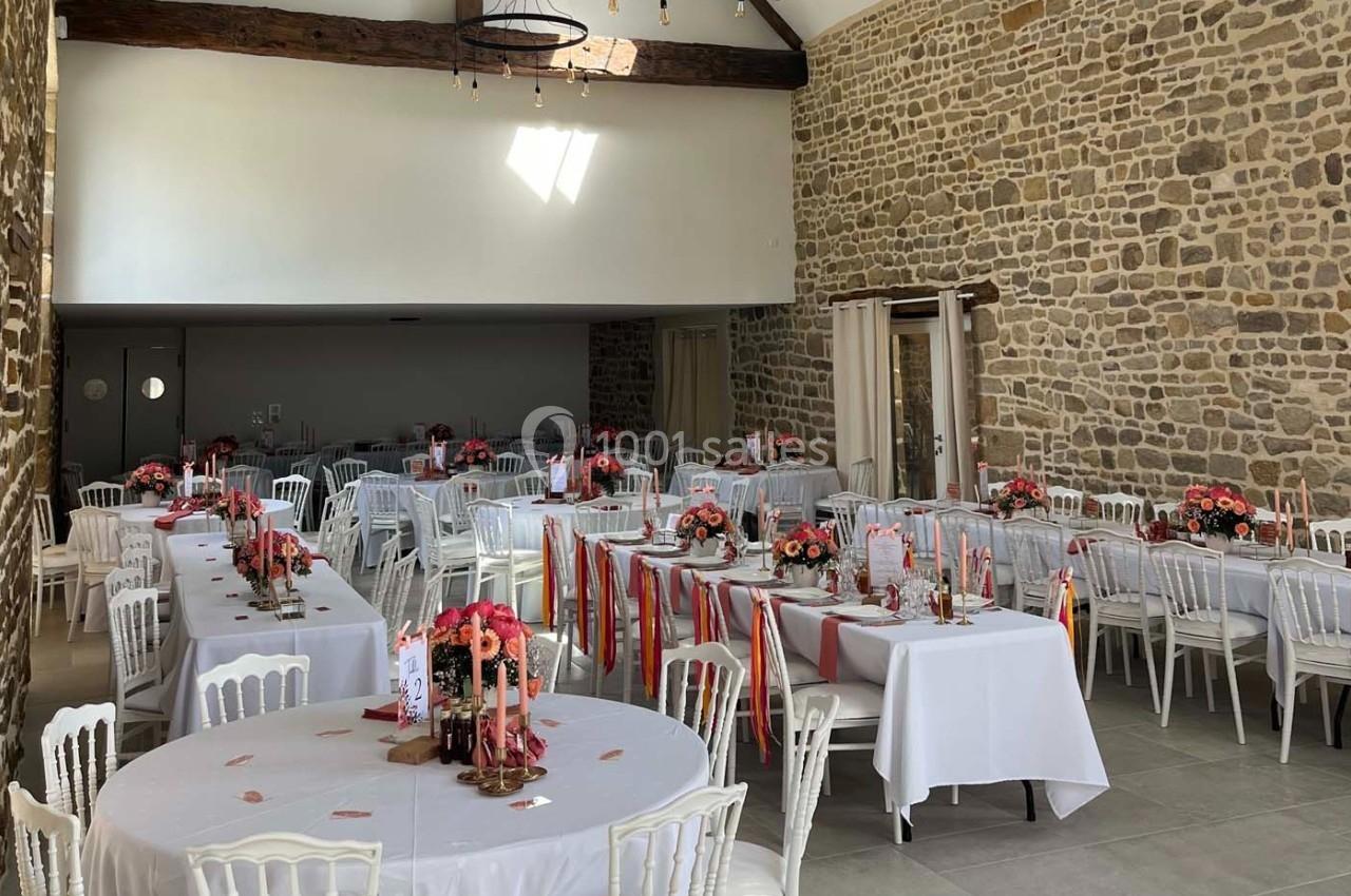 Salle de réception décorée pour un événement, avec tables dressées, nappes blanches et compositions florales colorées.