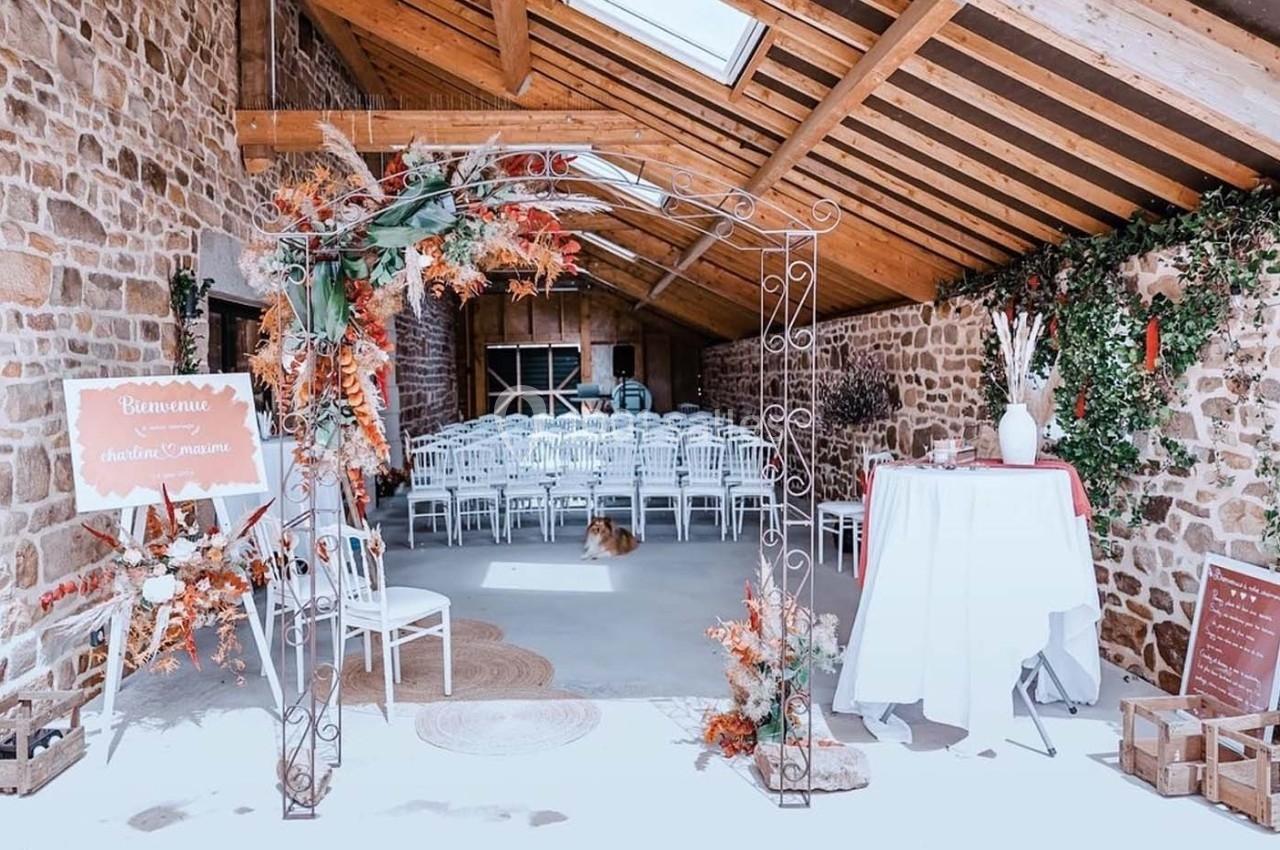 Salle de réception rustique avec des chaises blanches alignées, une arche décorée et des murs en pierre apparente.