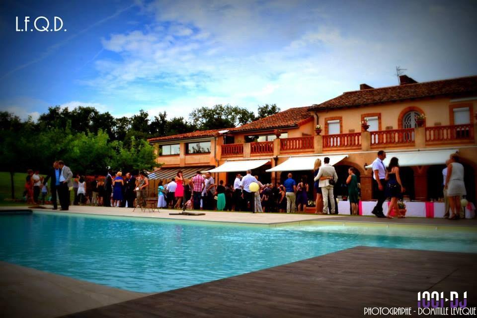Groupe de personnes rassemblées près d'une piscine devant une grande maison en briques sous un ciel dégagé.