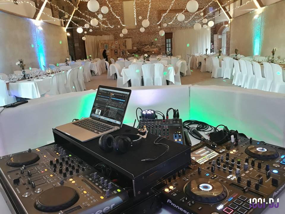 Vue d'une salle de réception décorée avec des guirlandes lumineuses, tables dressées et matériel de DJ au premier plan.