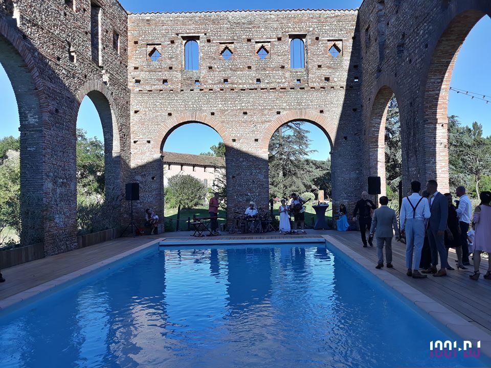 Piscine entourée d'arcades en briques dans un cadre extérieur avec des invités et un groupe de musique en arrière-plan.