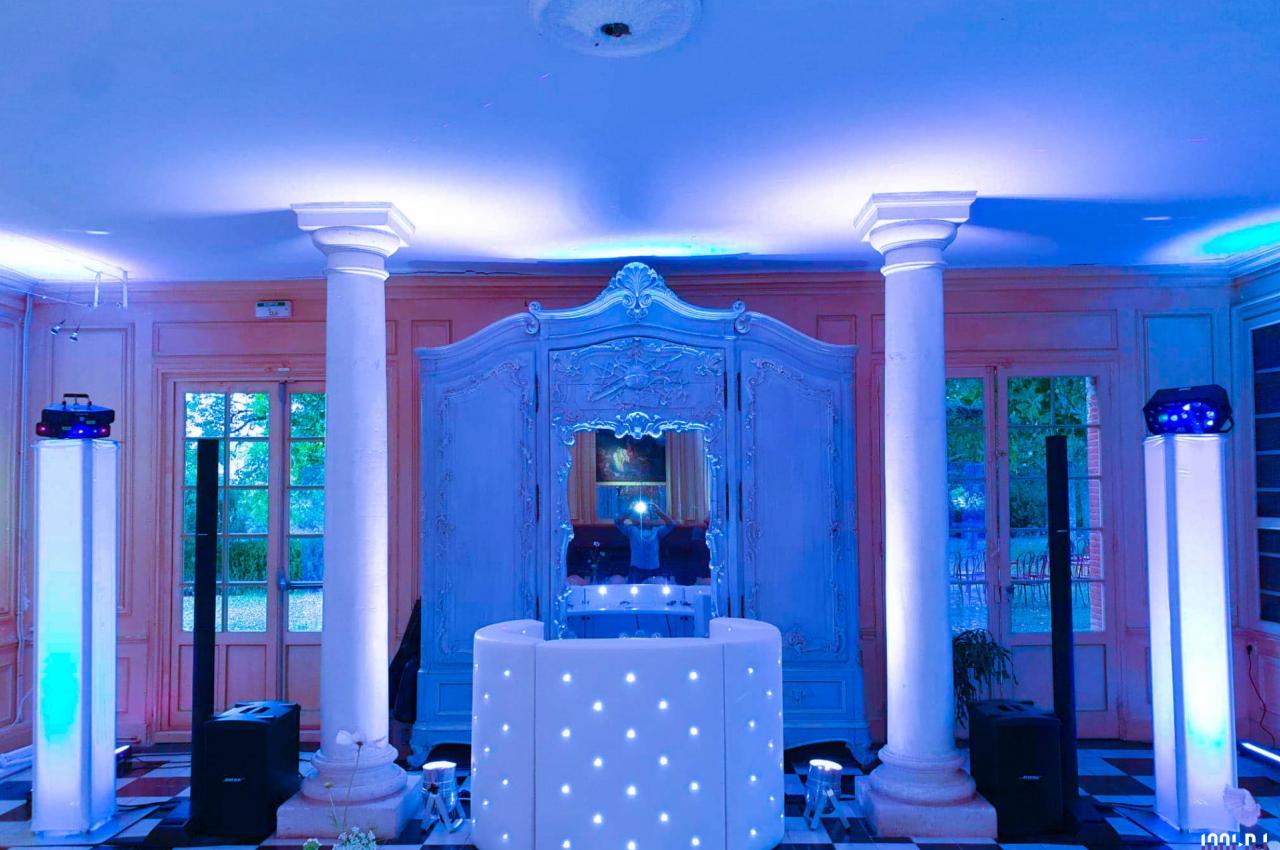 Salle élégante avec colonnes, éclairage bleu, mobilier lumineux et miroir orné au centre.