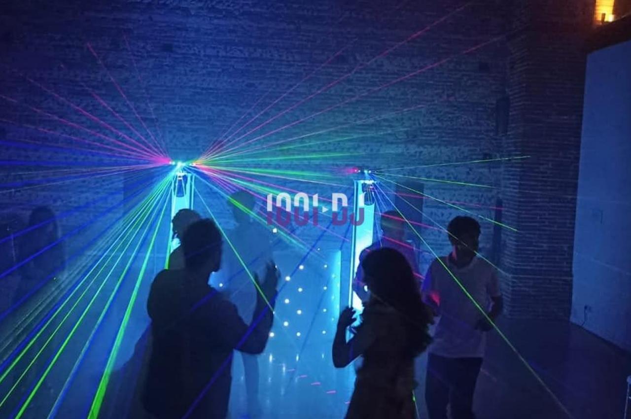 Des personnes dansent dans une salle sombre illuminée par des faisceaux laser colorés et un éclairage lumineux.