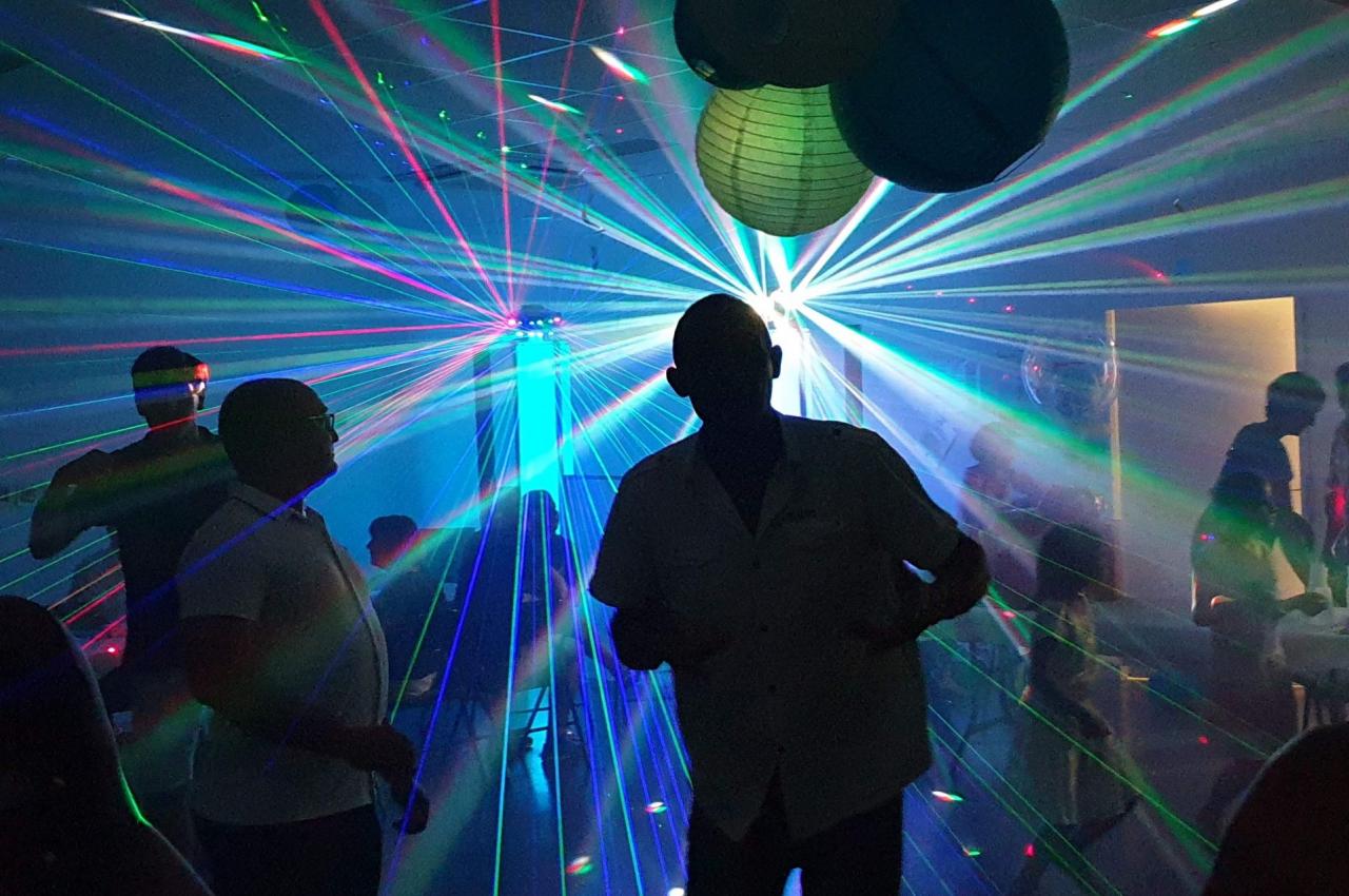 Personnes dansant dans une salle sombre illuminée par des faisceaux lumineux colorés et des décorations suspendues.