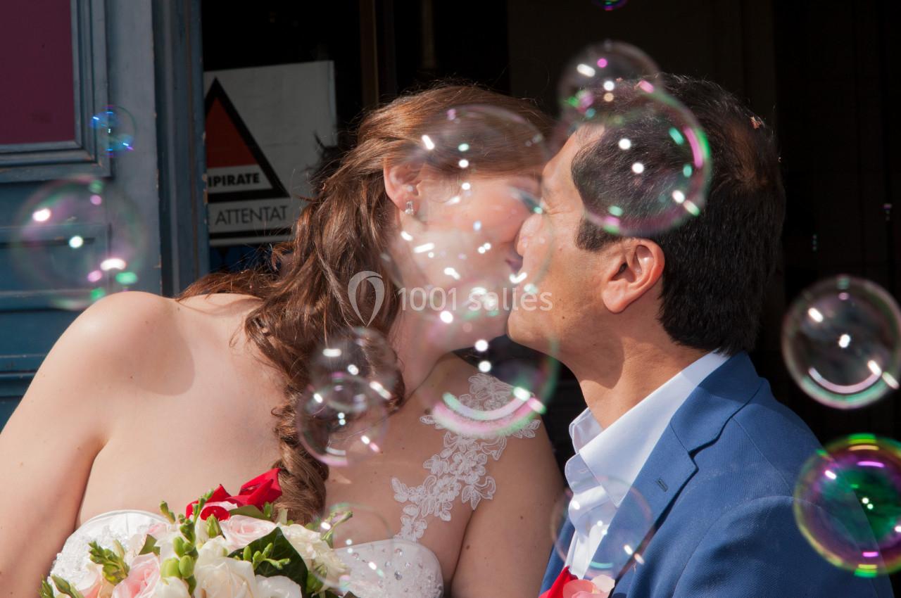 Un couple s'embrasse entouré de bulles de savon, la mariée tenant un bouquet de fleurs.