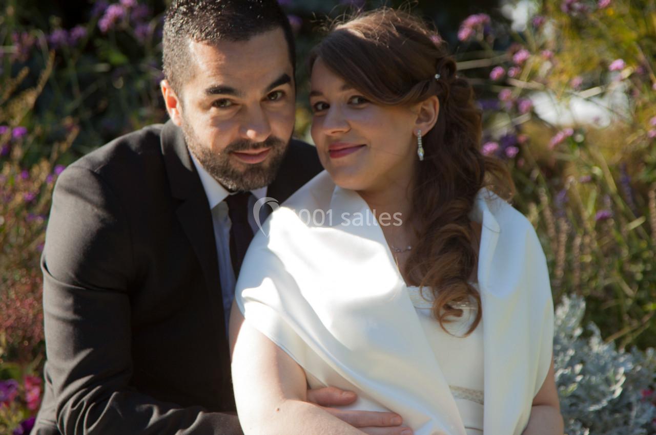 Un couple assis dans un jardin, habillé élégamment, souriant et entouré de végétation.