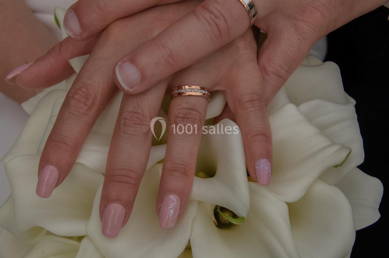 Mains d'un couple portant des alliances, posées sur un bouquet de fleurs blanches.