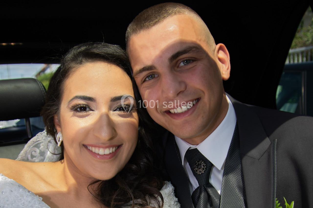 Un couple souriant en tenue de mariage, assis côte à côte dans une voiture.