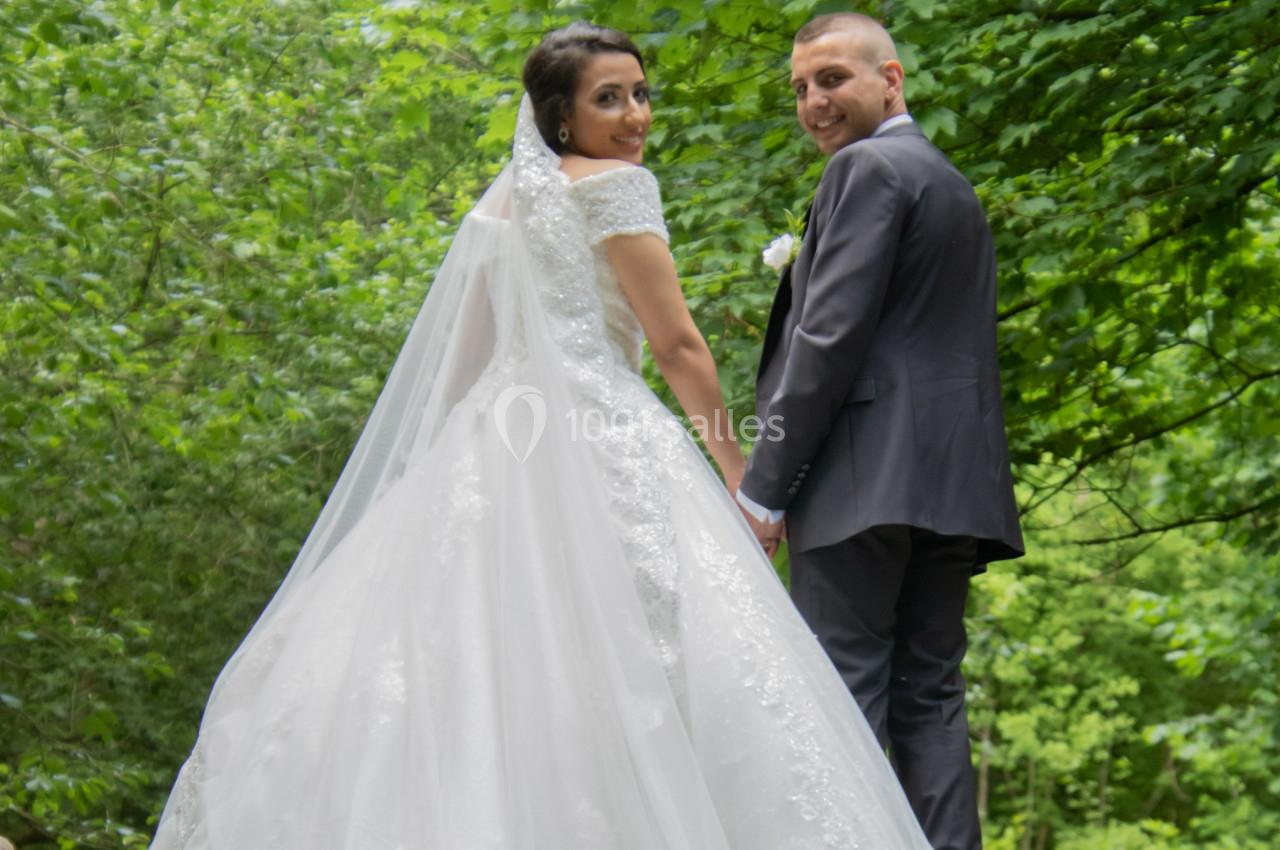 Un couple en tenue de mariage se tient dans un environnement verdoyant, regardant vers l'objectif.
