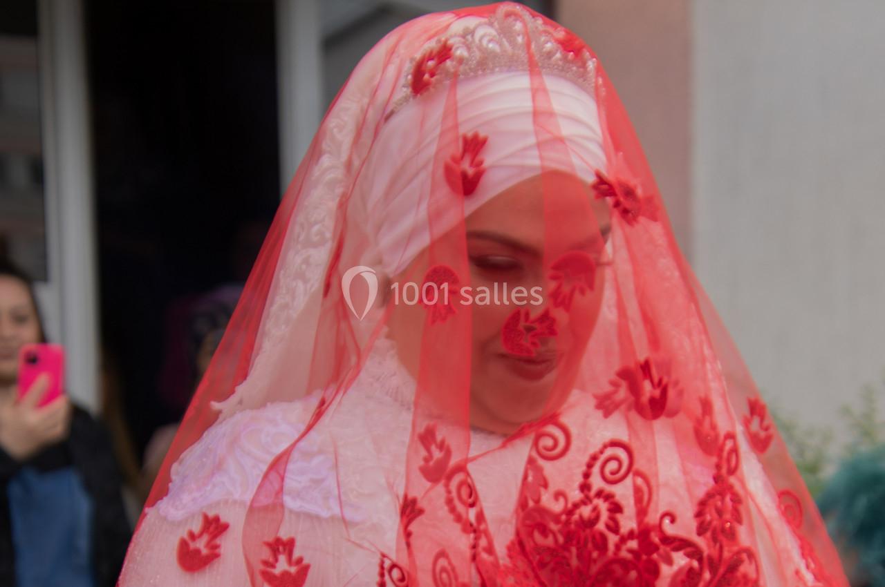 Femme portant un voile rouge orné de motifs floraux, vêtue de blanc, lors d'une cérémonie ou d'un événement festif.