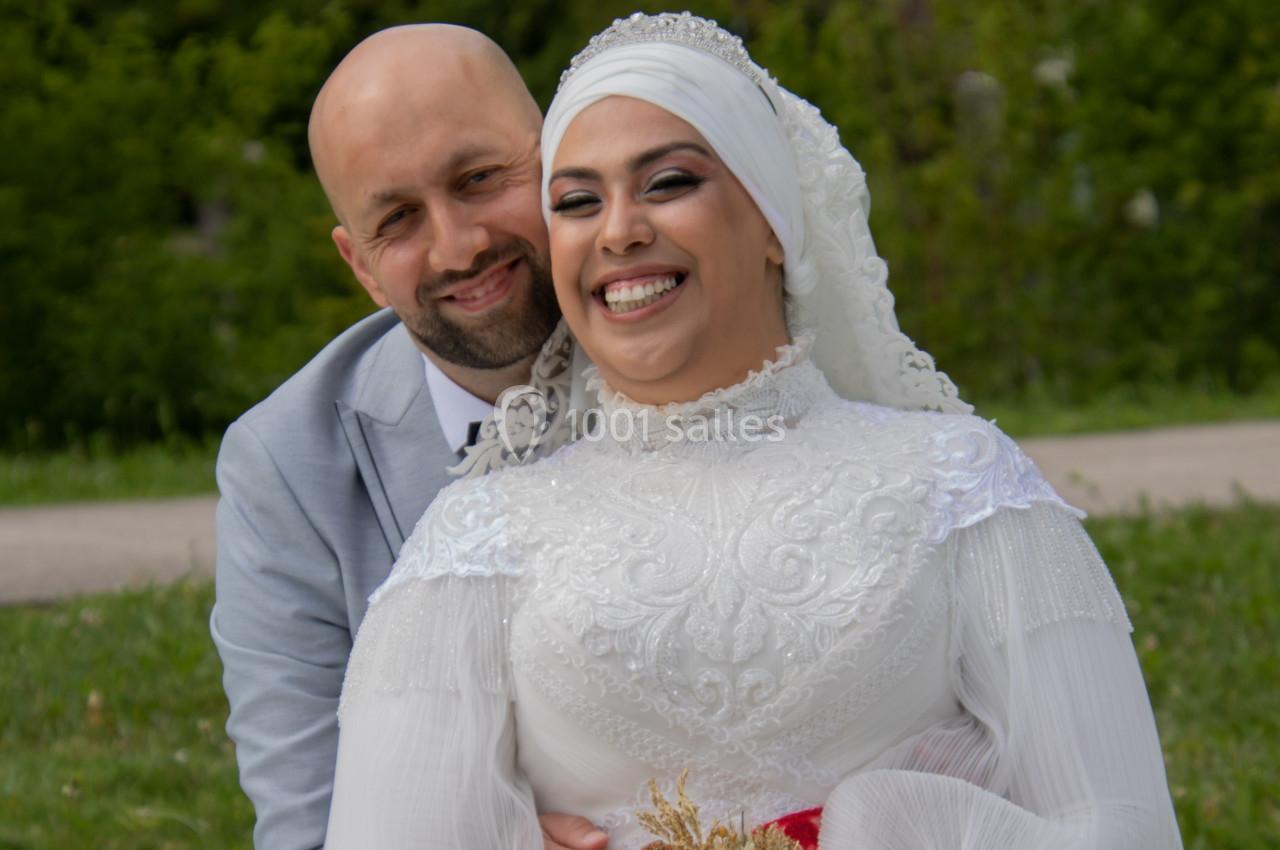 Un couple souriant en tenue de mariage, posant dans un parc verdoyant.