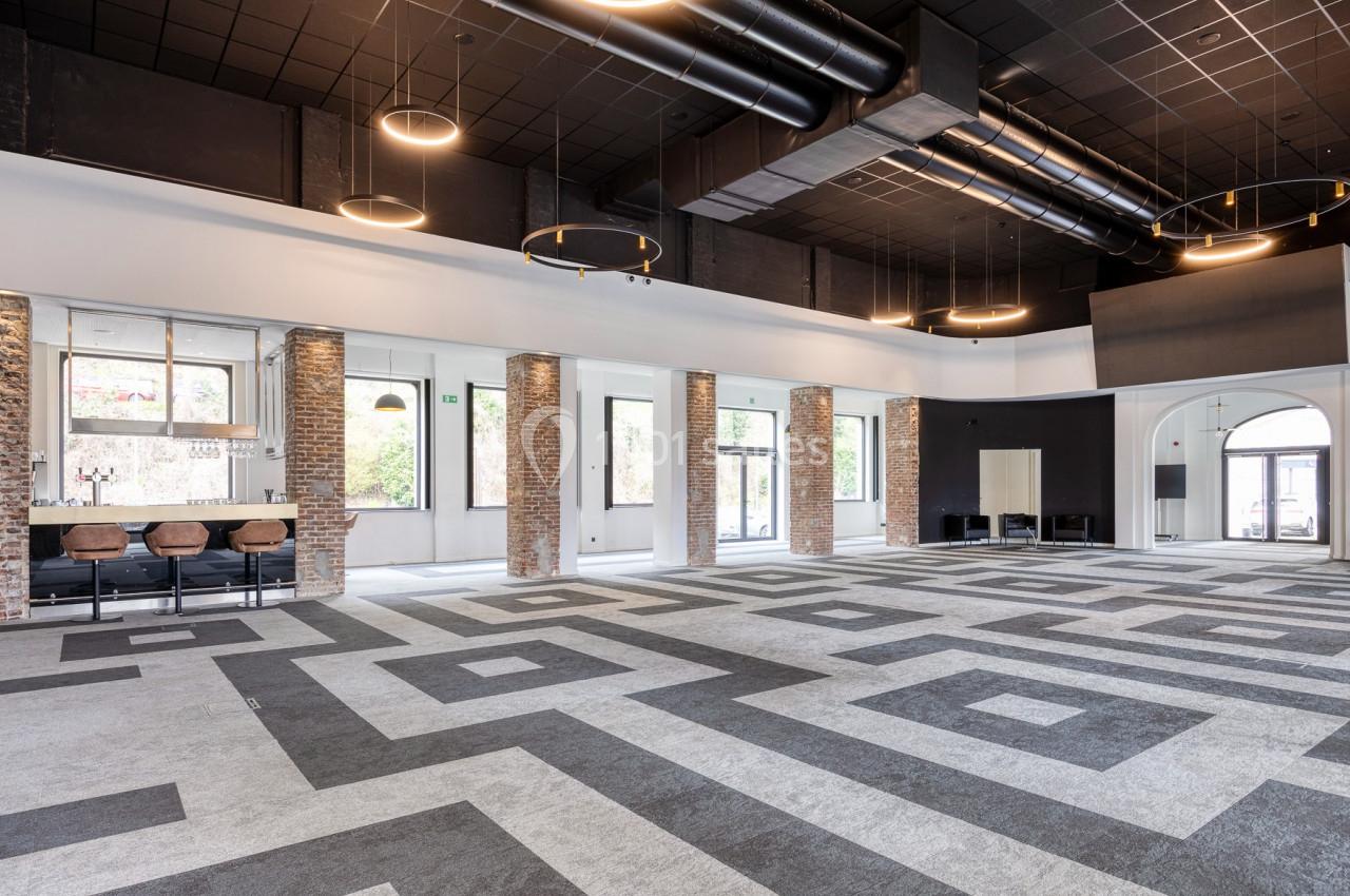 Salle spacieuse avec un sol à motifs géométriques, des murs en briques, un bar et des luminaires suspendus.