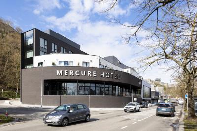 Façade moderne d'un hôtel Mercure avec des voitures circulant devant, entouré d'arbres et d'un ciel partiellement nuageux.