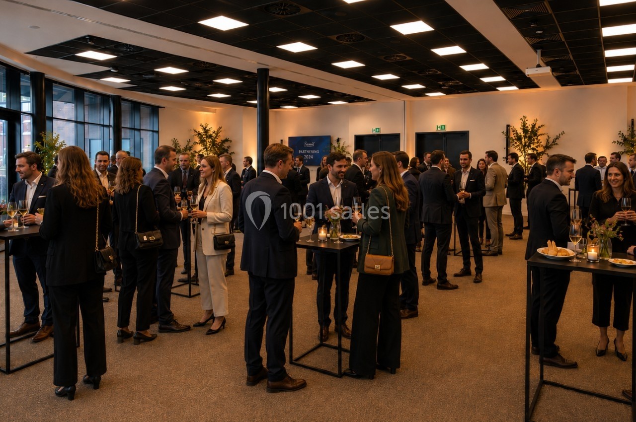 Des personnes en tenue professionnelle discutent debout autour de tables hautes dans une salle lumineuse.