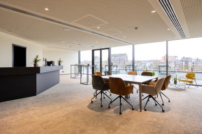 Terrasse moderne avec mobilier vert et blanc, vue sur une rivière et des bâtiments en arrière-plan.