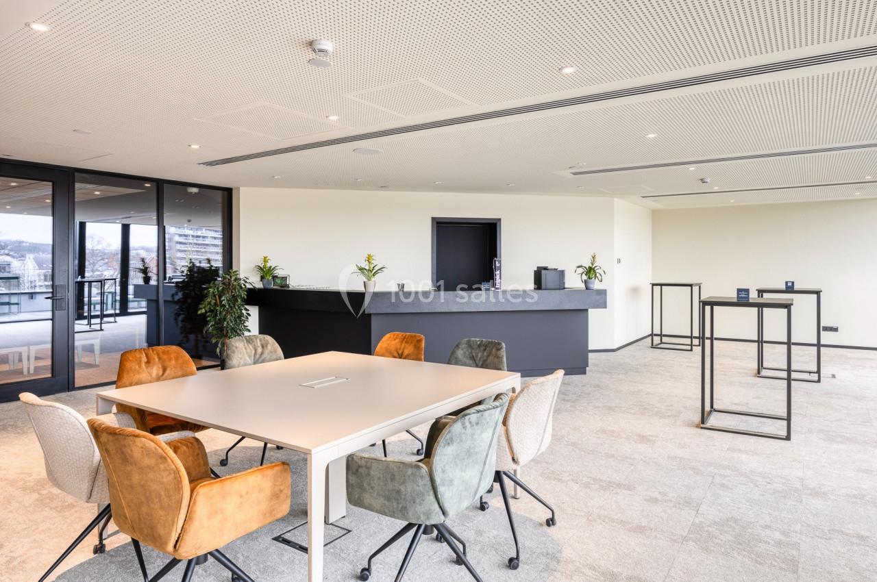 Salle de réunion lumineuse avec table centrale, chaises colorées et comptoir en arrière-plan.