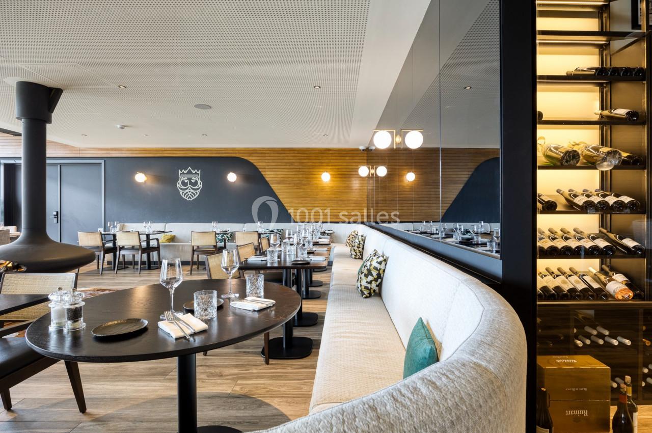 Salle de restaurant moderne avec tables dressées, banquettes, mur en bois, miroir et étagère à bouteilles de vin.