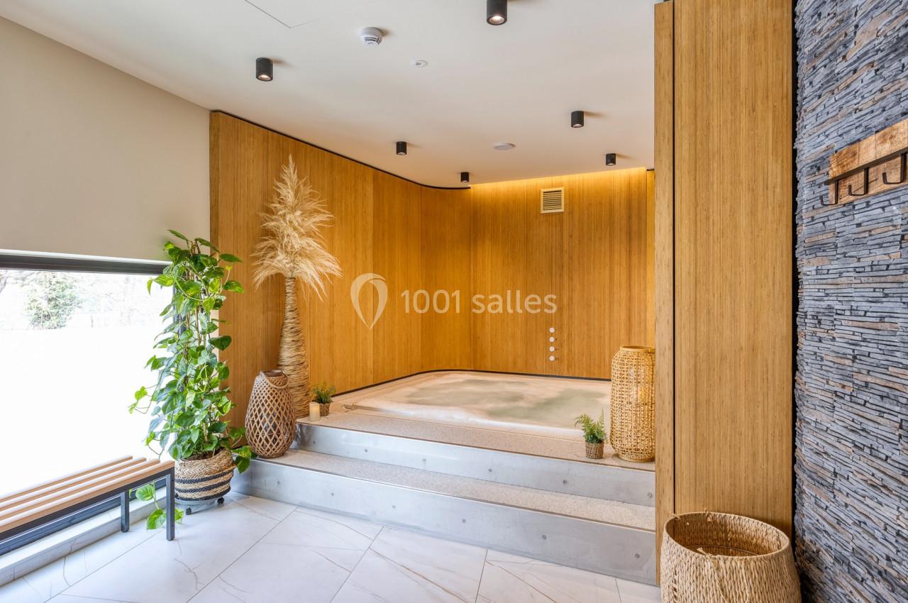 Bain à remous encastré dans une pièce au design naturel avec murs en bois, plantes et lumière douce.