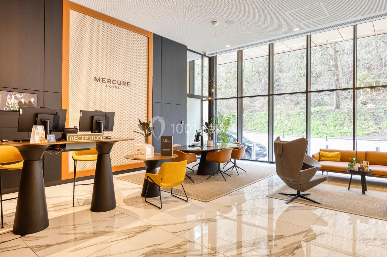 Hall d'accueil d'un hôtel moderne avec comptoirs de réception, fauteuils design et grandes baies vitrées.