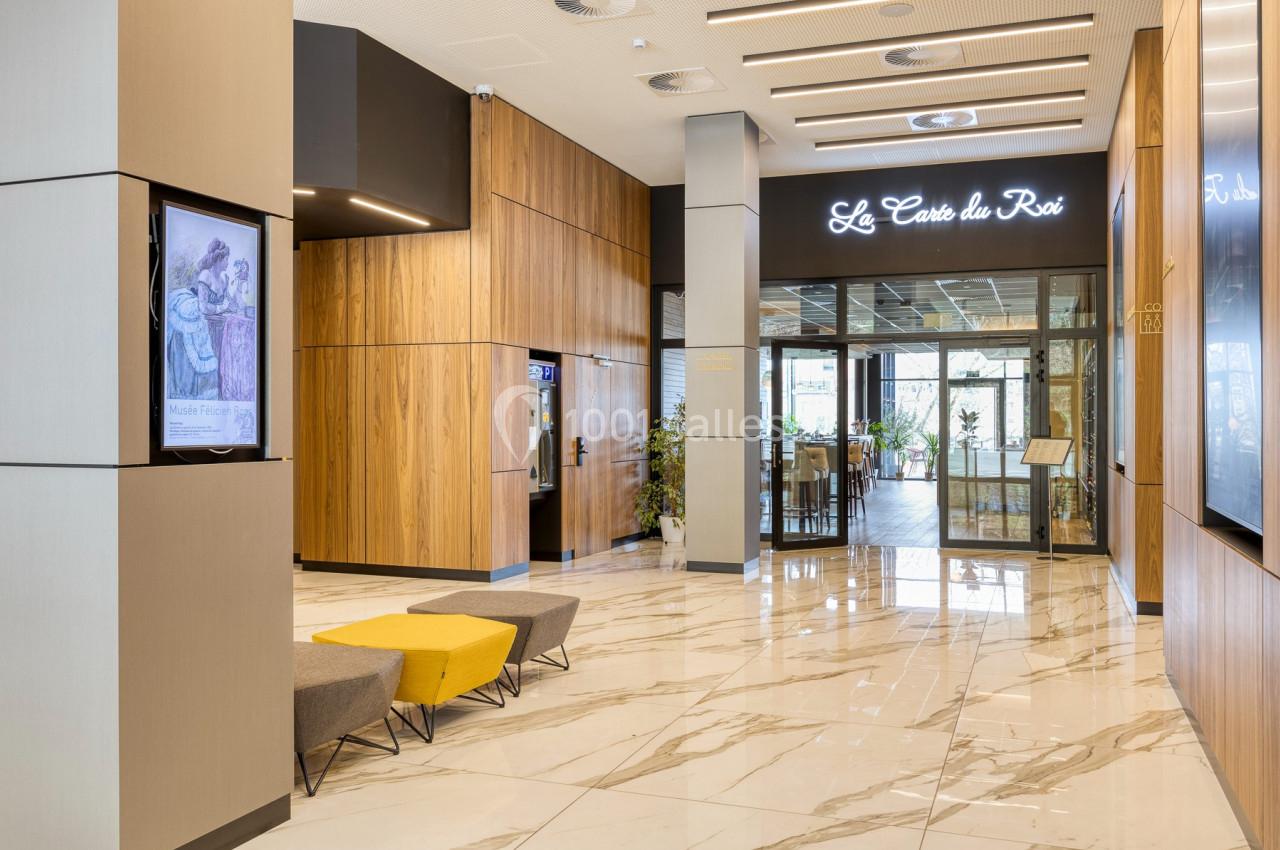 Entrée d'un restaurant avec sol en marbre, murs en bois, bancs jaunes et gris, et enseigne lumineuse.
