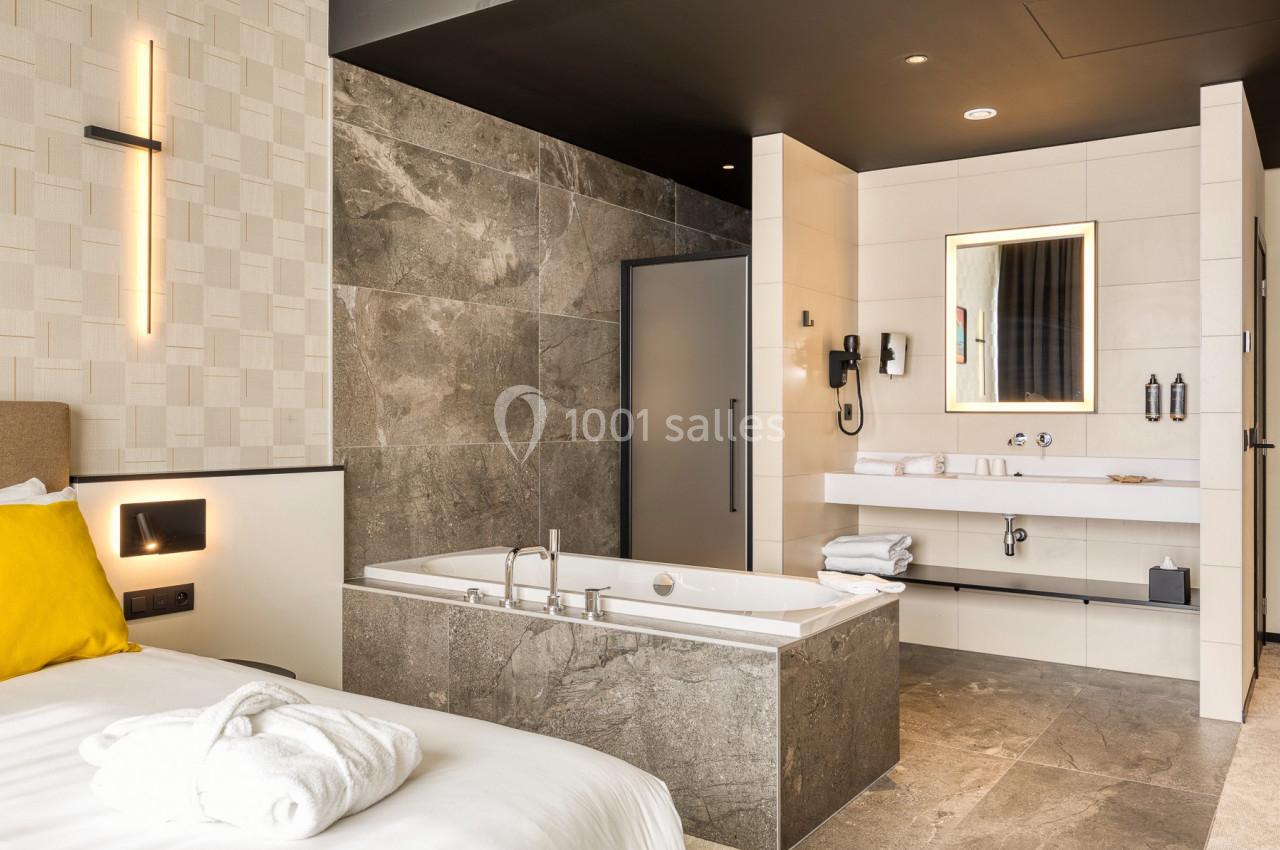 Salle de bain moderne avec baignoire en pierre, lavabo, miroir éclairé et décorations murales élégantes.