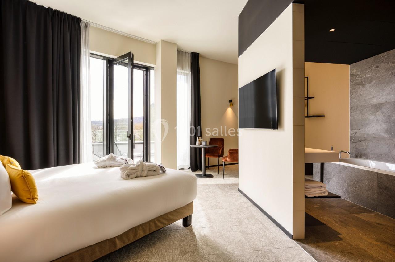 Chambre d'hôtel lumineuse avec lit double, télévision murale, salle de bain attenante et balcon avec vue extérieure.