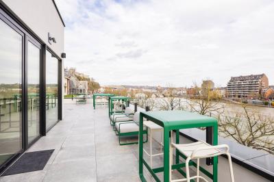 Terrasse moderne avec mobilier vert et blanc, vue sur une rivière et des bâtiments en arrière-plan.
