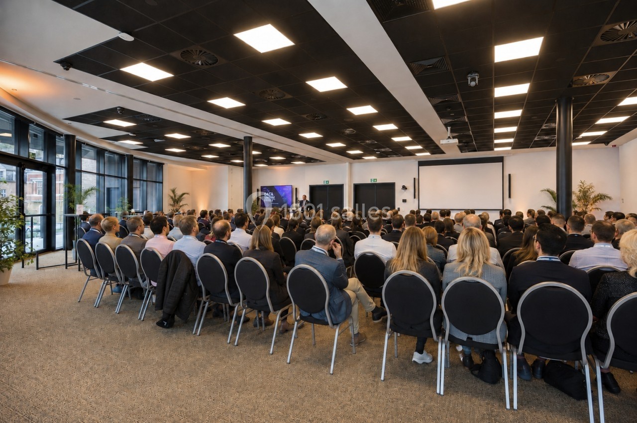 Salle de conférence avec un public assis face à un orateur et un écran de présentation.