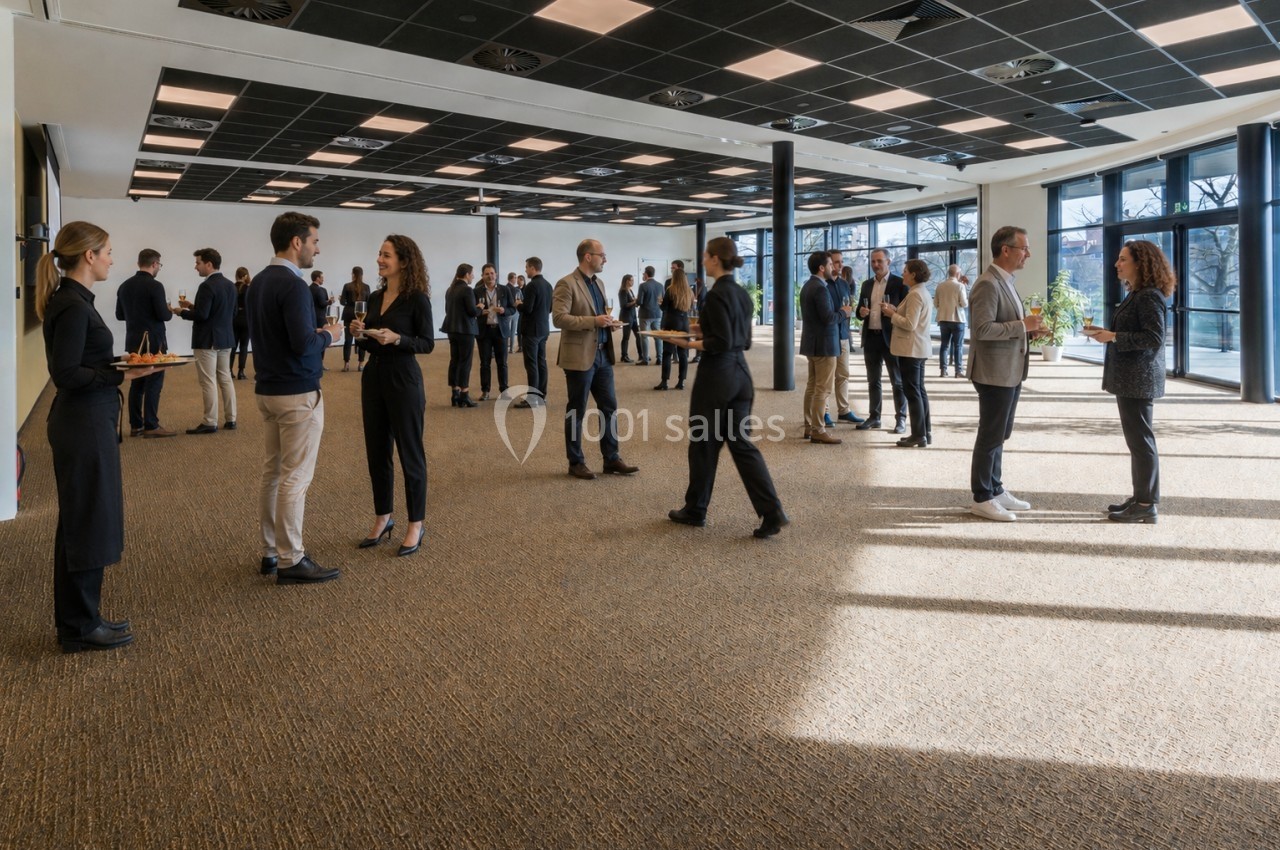 Des personnes discutent debout dans une grande salle lumineuse, avec des serveurs apportant des plateaux.