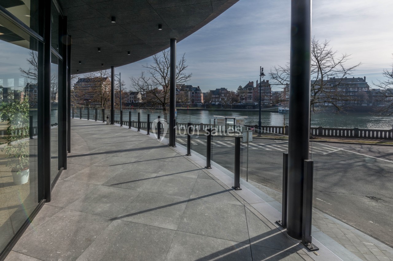 Terrasse moderne avec garde-corps en verre, vue sur une rivière bordée de bâtiments et d'arbres en hiver.