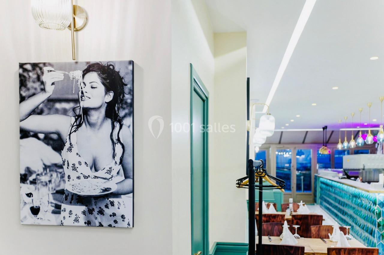 Photographie en noir et blanc d'une femme accrochée au mur d'un restaurant lumineux avec des tables et un bar.