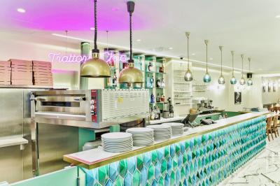 Salle de restaurant lumineuse avec tables en bois dressées, plafond décoré de guirlandes végétales et grandes baies vitrées.