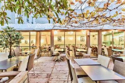 Salle de restaurant lumineuse avec tables en bois dressées, plafond décoré de guirlandes végétales et grandes baies vitrées.