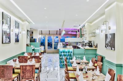 Salle de restaurant lumineuse avec tables en bois dressées, plafond décoré de guirlandes végétales et grandes baies vitrées.