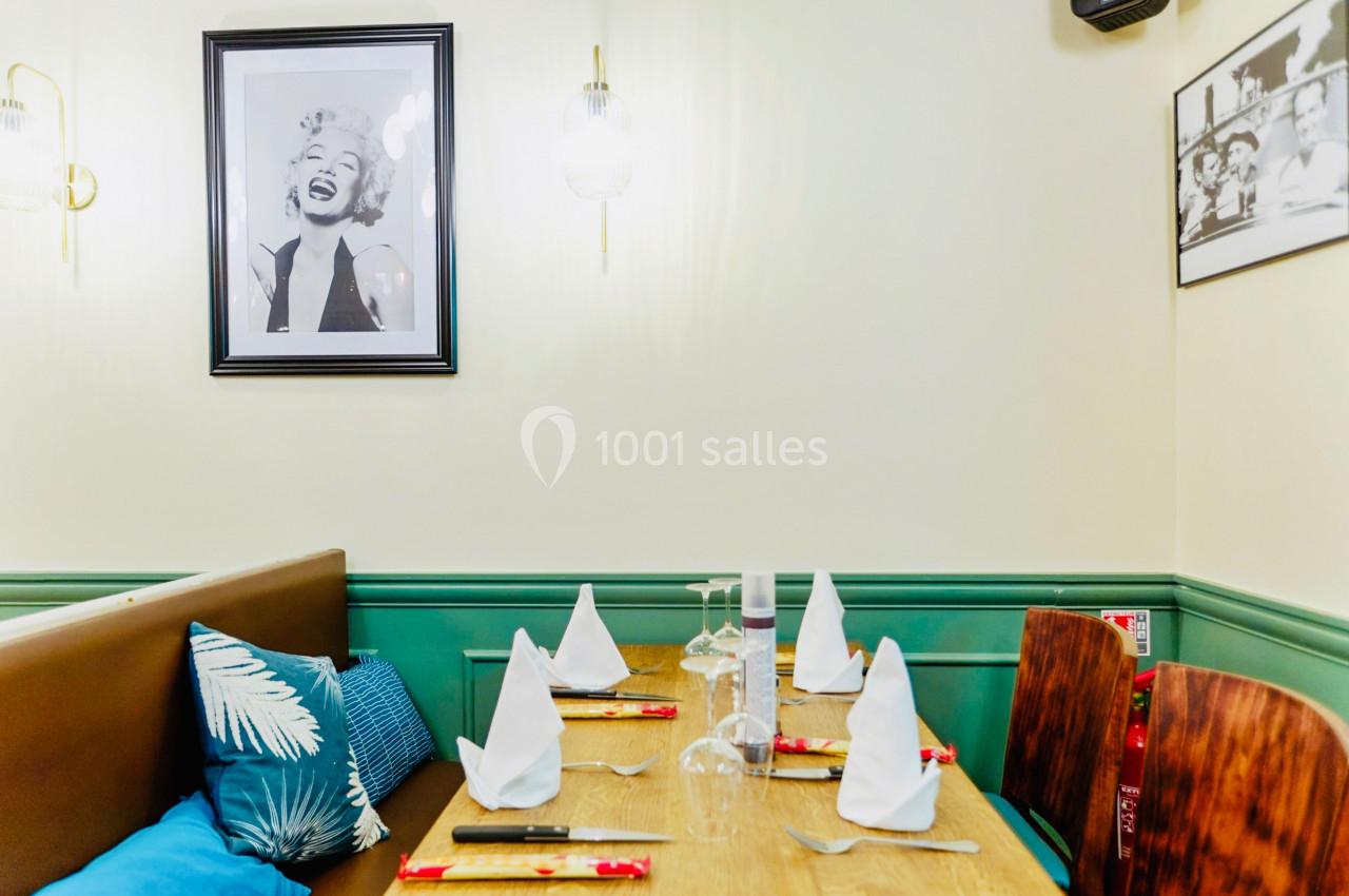 Table dressée avec serviettes pliées, verres et couverts, dans un restaurant décoré avec des photos au mur.