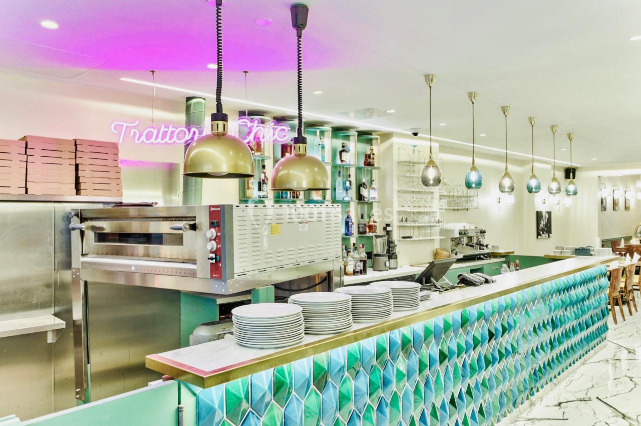 Comptoir de restaurant avec carrelage coloré, four à pizza, étagères de bouteilles et luminaires suspendus.