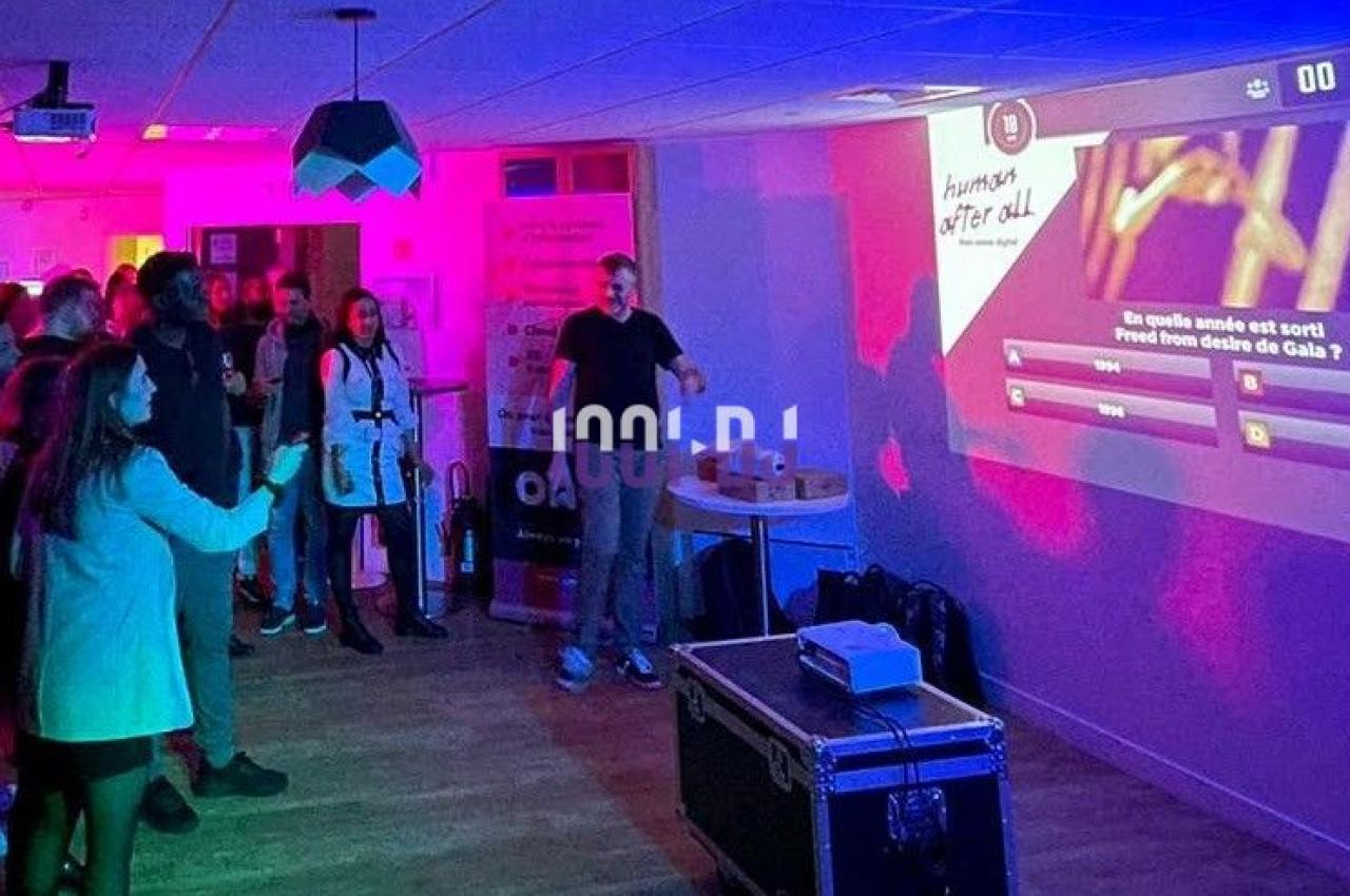 Un groupe de personnes participe à un quiz interactif projeté sur un mur dans une salle éclairée par des lumières colorées.