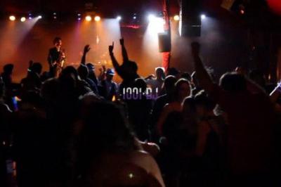 Un DJ mixe sur scène devant un écran géant projetant une vidéo d'une danseuse en tenue scintillante.