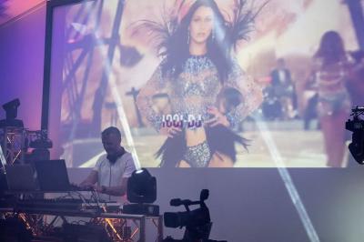 Un DJ mixe sur scène devant un écran géant projetant une vidéo d'une danseuse en tenue scintillante.