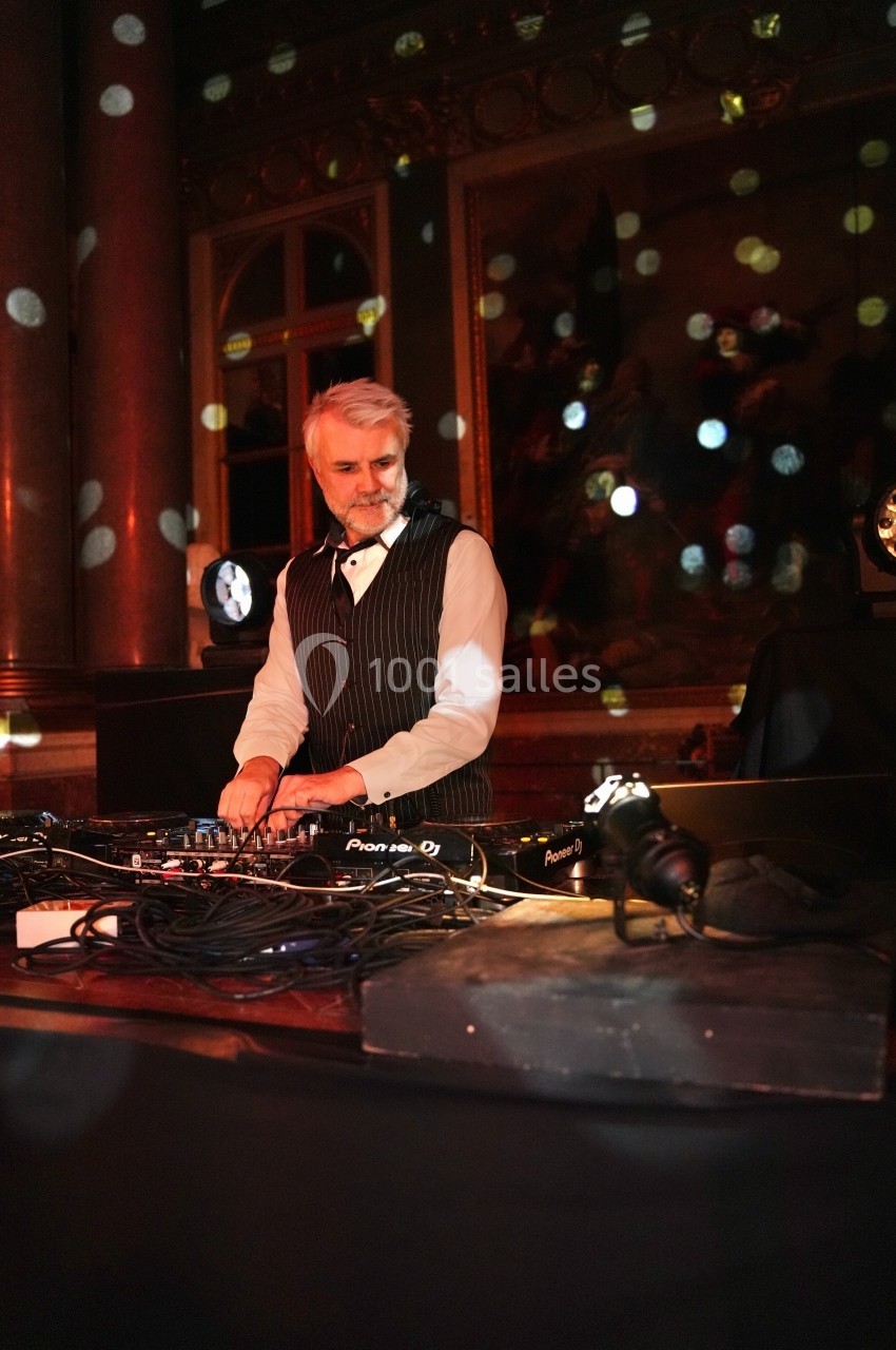 Un homme en costume joue de la musique sur une table de mixage dans une salle éclairée par des lumières colorées.