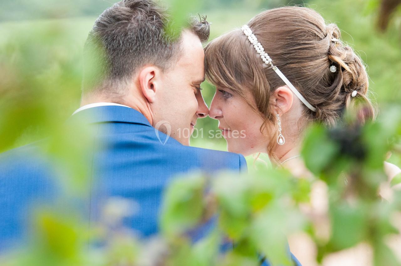 Un couple se regarde tendrement dans un cadre naturel avec des feuilles floues au premier plan.