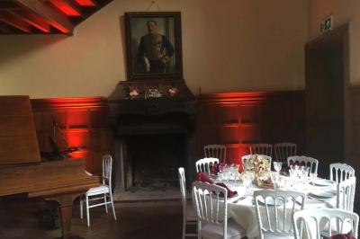 Salle de réception élégante avec tables dressées, chaises blanches, décorations florales et un piano en arrière-plan.