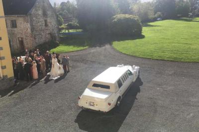 Salle de réception élégante avec tables dressées, chaises blanches, décorations florales et un piano en arrière-plan.