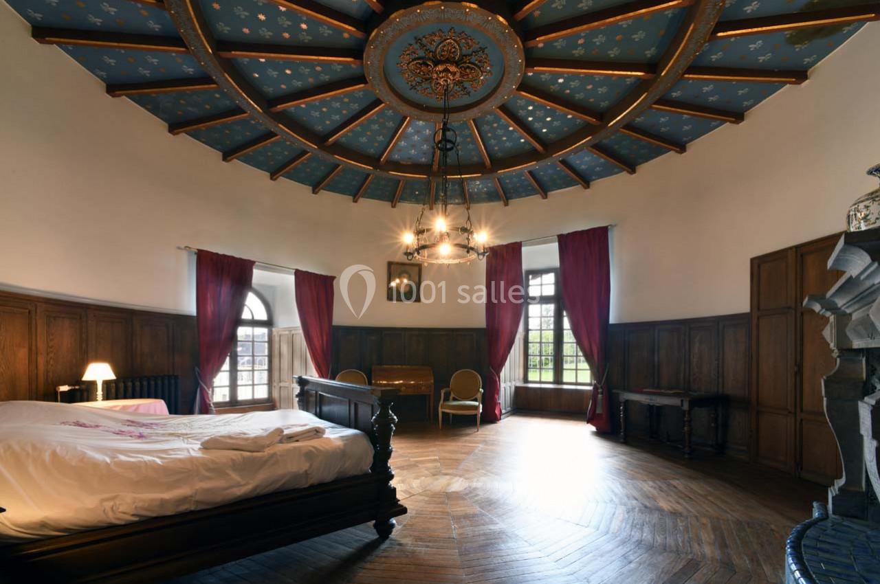 Chambre spacieuse avec lit en bois, plafond décoré, parquet, rideaux rouges et grande fenêtre laissant entrer la lumière.
