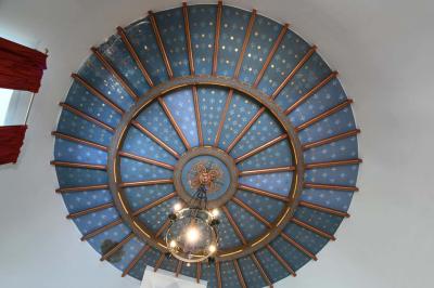 Salle de réception élégante avec tables dressées, chaises blanches, décorations florales et un piano en arrière-plan.