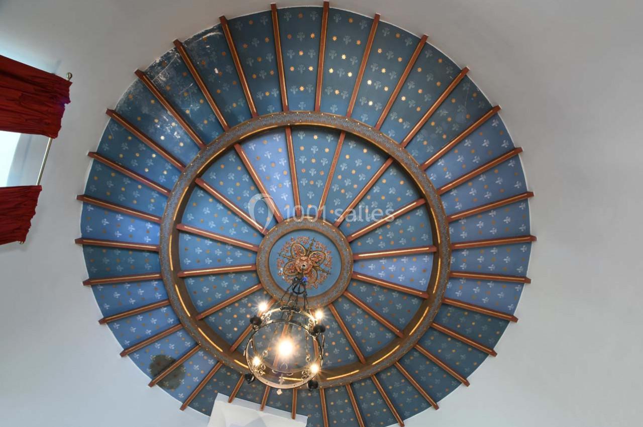 Plafond voûté bleu orné d'étoiles dorées, avec une suspension centrale et des poutres en bois rayonnantes.