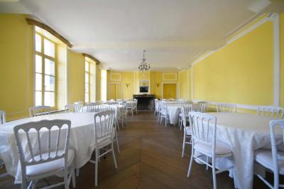 Salle de réception élégante avec tables dressées, chaises blanches, décorations florales et un piano en arrière-plan.