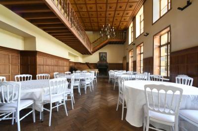 Salle de réception élégante avec tables dressées, chaises blanches, décorations florales et un piano en arrière-plan.